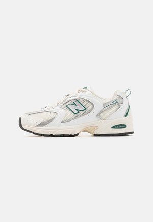 Witte New Balance 530 sneakers met meshpanelen, groene accenten, verstevigde hiel en zwarte rubberen buitenzool. Vetersluiting met logodetail.