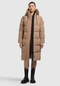 Manteau en duvet beige avec capuche, doté d'une fermeture éclair à l'avant, de boutons-pression et de poches latérales ; design matelassé pour l'isolation. Accents noirs sur les fermetures éclair.