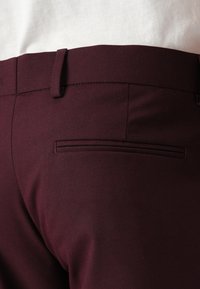Bordeauxfarbene Hosen aus glattem Stoff, mit slim fit, flachem Vorderteil und einem Gesäßtasche mit sauberem Nahtabschluss.