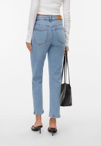 Svetlo modri jeans z ravnim krojem, petimi žepi in usnjenim paščkom na zadnjem pasu, nosijo z črnimi sandali na peto.