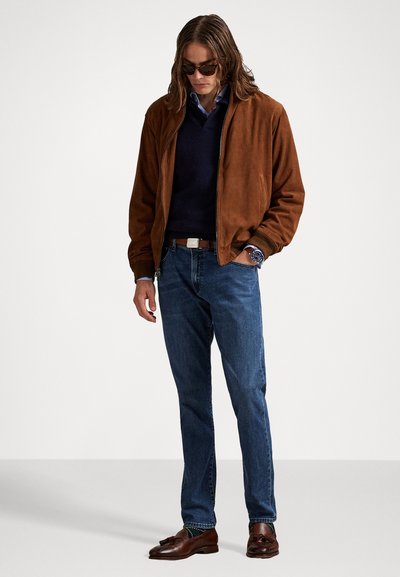 Prune suede bomber-jakk üle tumesinise sviitri, siniste teksade ja pruunide kingade. Aksessuaaride hulka kuuluvad prillid ja randmevaat.