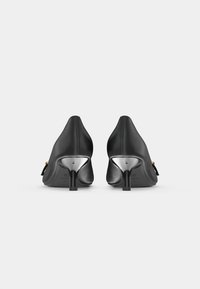 Sapatos de salto alto em couro preto com um design elegante, bico alongado e detalhes metálicos em um salto curvado. Sola preta plana.