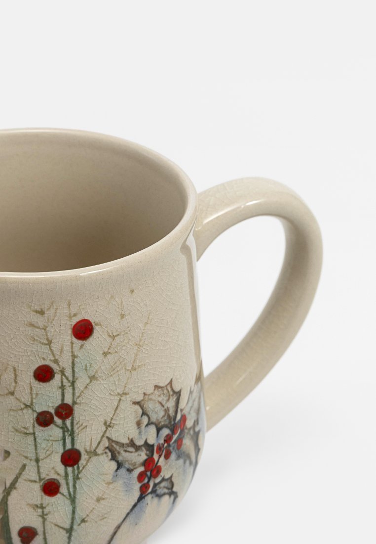 Keramiktasse mit einer beigen, strukturierten Oberfläche, verziert mit dekorativem Stechpalmenblatt und roten Beeren sowie einem stabilen, gebogenen Henkel.