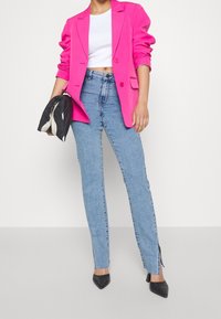 Fuchsiarosa skräddarsydd blazer över en vit crop top, kombinerad med ljusblå högmidjade jeans med sidorskärningar och spetsiga svarta klackar.