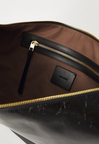 Black leather bag interior with brown fabric lining. Includes a zip pocket, gold zipper, and branded black leather tag. Smooth texture.