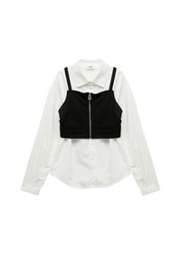 Top corto nero con bretelle regolabili sopra una camicia bianca a maniche lunghe, caratterizzato da una cerniera anteriore e due piccole tasche frontali.