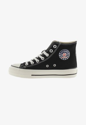 Zwarte high-top sneaker van canvas met witte veters, rubberen neuskap en een ronde logopatch met "Victoria" en "Since 1975."