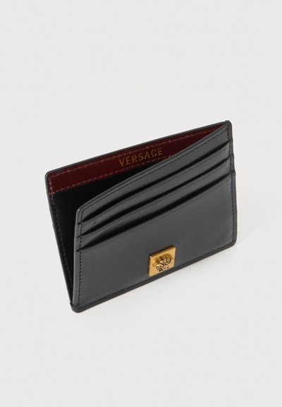 Porte-cartes en cuir noir avec emblème Méduse doré, plusieurs emplacements pour cartes, et intérieur bordeaux embossé du nom "VERSACE" en lettres dorées.