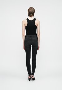 Camisola preta justa combinada com jeans pretos de cintura alta. Os jeans apresentam bolsos traseiros, um corte slim e um leve detalhe desfiado na bainha.