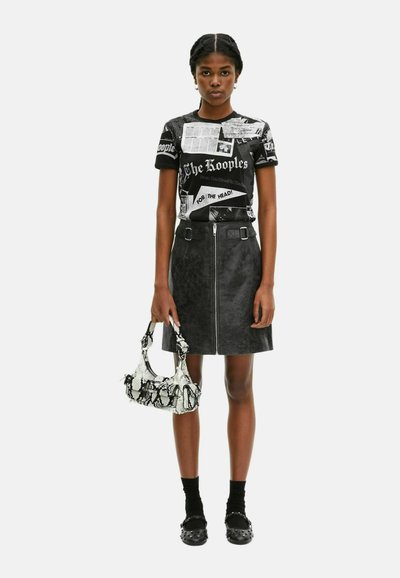 Zwarte t-shirt met grafische prints, gecombineerd met een zwarte nepleer rok met een rits aan de voorkant. Accessoires omvatten een tas met slangenhuidpatroon.