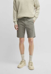 Pantaloni corti grigi in tessuto testurizzato, abbinati a un maglione a coste beige chiaro e sneakers beige dal design minimalista.