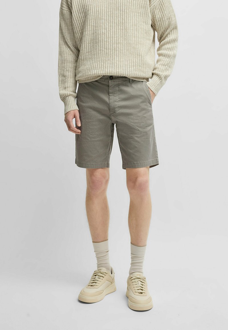 Pantaloni corti grigi in tessuto testurizzato, abbinati a un maglione a coste beige chiaro e sneakers beige dal design minimalista.