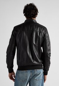 Schwarze Leder-Bomberjacke mit gerippten Bündchen und Saum, die eine glatte Textur und ein strukturiertes Design aufweist, von hinten fotografiert.