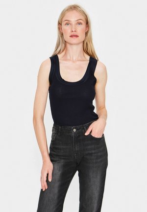 Sort ribbet tanktop med en scoop-udskæring, parret med mørke jeans med forlommer og en formsyet silhuet. Flad tekstur, afslappet stil.