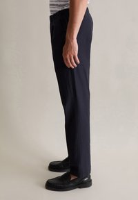 Navyblauwe broek met een ontspannen pasvorm, elastische tailleband en zijzakken, gecombineerd met zwarte loafers. Soepele textuur en recht gesneden ontwerp.