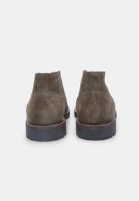 Stivaletti alla caviglia in suede marrone con punta rotonda, texture liscia, pannelli laterali elastici e suola scura a contrasto. Dettagli cuciti vicino al tallone.