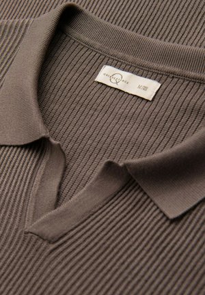 Bruin geribd poloshirt met een omslagkraag, voorzien van een label op de hals dat maat medium aangeeft. Zachte textuur, minimaal ontwerp.