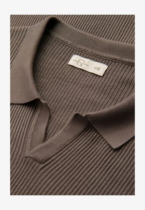 Maglietta polo marrone a coste con colletto ripiegato, dotata di un'etichetta sul collo che indica la taglia media. Texture morbida, design minimal.