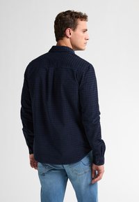 Marine geblokte blouse met lange mouwen, gestructureerde stof, knopenmanchetten, yoke detail op de rug, gecombineerd met lichtblauwe spijkerbroek.