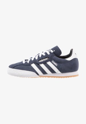 Baskets Adidas Samba, dessus en suede bleu marine avec des accents en cuir blanc, trois rayures blanches, semelle en caoutchouc texturée et col rembourré.