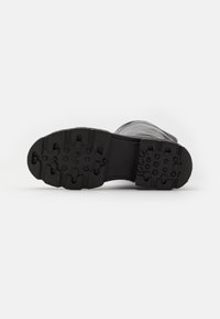 Czarna podeszwa buta z teksturowanej gumy, z wypukłymi okrągłymi i prostokątnymi wzorami zapewniającymi przyczepność; płaski, zaokrąglony kształt palców.