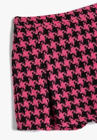 Tessuto a motivi rosa e nero, con un design a scacchi houndstooth, dalla superficie testurizzata e un bordo piegato visibile nella parte superiore.