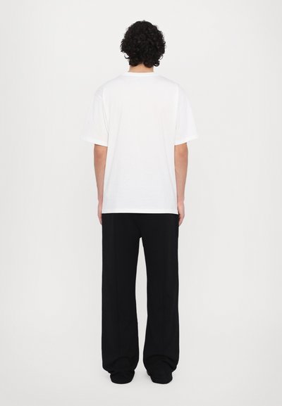 T-shirt en coton blanc à manches courtes et col rond, associé à un pantalon noir ample, vu de dos.