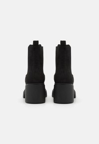Botines de ante negros con tacón robusto, que cuentan con una textura suave, paneles laterales elásticos y tiradores para ponerlos y quitarlos con facilidad.