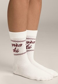 Białe skarpetki do kostki z czerwonym wzorem dzianym oraz napisem „happy” i „ski”. Mankiet prążkowany, gładka faktura. Standardowy kształt skarpetek.