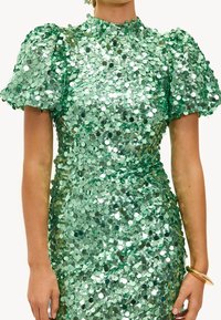 Vestido verde de lentejuelas con cuello alto y mangas abullonadas. El vestido tiene una silueta ajustada y brilla con acentos metálicos.