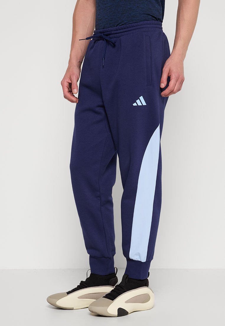 Navyblauwe sweatpants met een lichtblauwe zijpaneel, elastische tailleband en zijzakken. Heeft een witte Adidas-logo.
