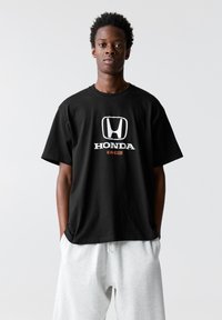 Čierne bavlnené tričko s bielym logom Honda a textom "CIVIC" v oranžovej farbe. Strih je voľný, s krátkymi rukávmi a okrúhlym výstrihom.