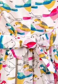 Biała sukienka z tkaniny z nadrukiem ptaków w kolorach różowym, żółtym, niebieskim i zielonym. Posiada kokardę w talii oraz detalowane plisowanie spódnicy.