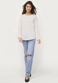 Long-sleeve light beige top paired with ripped light blue jeans and black flats. The top has a round neckline and a relaxed fit.