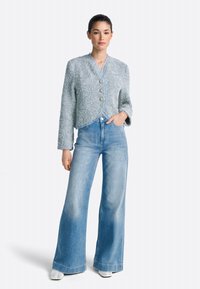 Texturált, világoskék rövidített dzseki kerek gallérral, három gombbal és rojtos szegéllyel, magas derekú, széles szárú farmernadrággal párosítva.