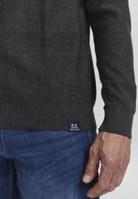 Mørk grå strikkegenser med ribbet kant og mansjetter. Har et lite merke på siden. Brukt med blå denimjeans.