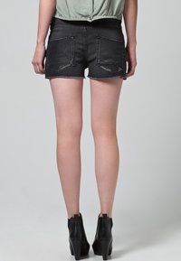 Pantalones cortos de mezclilla negros con dobladillos deshilachados, bolsillos traseros y detalles de costura visibles, combinados con botas negras de tacón alto.