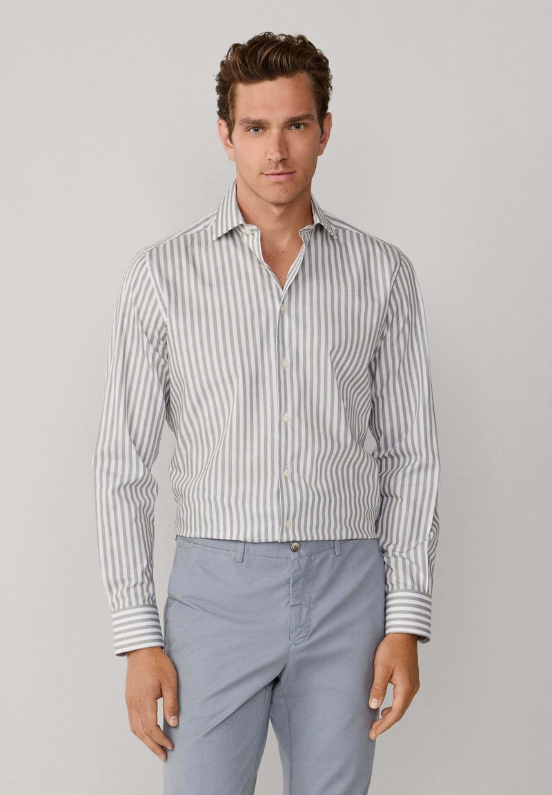 Weißes Langarmhemd mit dünnen grauen vertikalen Streifen, Kentkragen und kontrastierenden gestreiften Manschetten, kombiniert mit hellblauen Hosen.