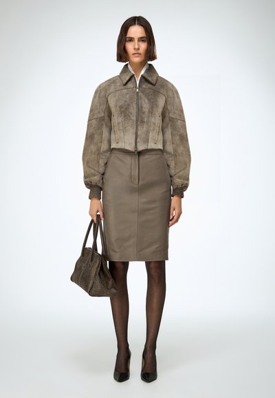 Smeđa bomber jakna od brušene kože s naduvenim rukavima, u kombinaciji s uskom maslinasto zelenom kožnom suknjom. Ukrašeno smeđom torbom i crnim salonkama.