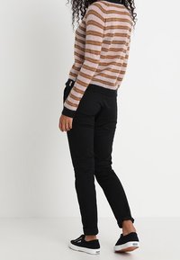 Sweter w paski w odcieniach beżu i brązu, z okrągłym dekoltem i ściągaczami; zestawiony z czarnymi dopasowanymi spodniami i czarnymi sneakersami.