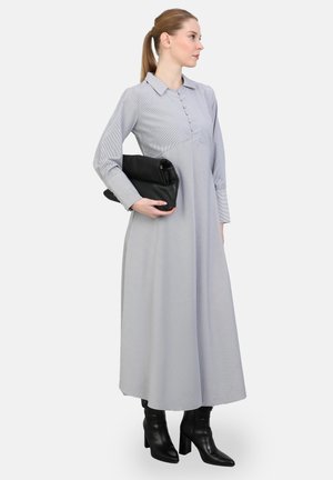 Long, light gray dress with a collar and front button closure; features long sleeves and a textured fabric. Black clutch and heeled boots.