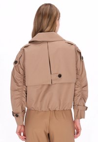 Khaki cropped jack met een hoge kraag, geplooide mouwen en een plooi aan de achterkant, met knoopaccenten op de schouders en manchetten.