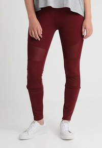 Bordó leggings rugalmas anyagból, hálós betétekkel és testhezálló kialakítással, fehér perforált sportcipővel párosítva.