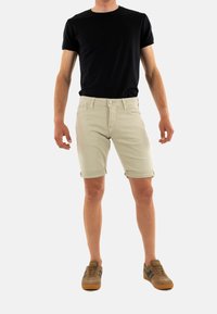Beige shorts met opgerolde boorden, gecombineerd met een zwart t-shirt en bruine sneakers. De shorts hebben een klassiek vijf-pocket ontwerp en een aansluitende taille.