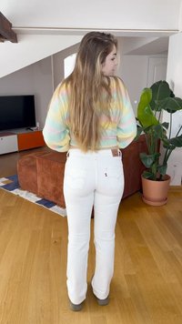 Jeans blancs évasés avec une taille haute et des poches arrière, associés à un pull pastel tie-dye. Canapé en velours côtelé texturé et plante en pot en arrière-plan.