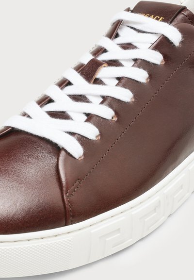 Baskets en cuir marron avec des lacets blancs et une semelle blanche épaisse présentant un motif géométrique le long du bord.