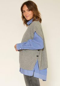 Gilet en tricot gris clair à manches courtes superposé sur une chemise boutonnée rayée bleu et blanc. Dispose de boutons sur les côtés et d'une coupe décontractée.