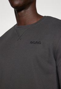 Maglietta a maniche lunghe grigio scuro con collo rotondo e un delicato dettaglio di cucitura incrociata, dotata di un logo ricamato "BORG" sul petto.