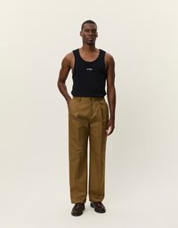 Fekete pamut ujjatlan póló fehér logóval, magas derekú, egyenes szabású khaki nadrággal párosítva. Barna, strapabíró cipők teszik teljessé a megjelenést.