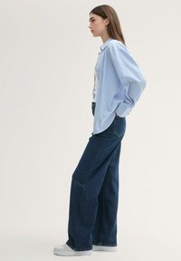 Camisa a rayas azul claro con corte holgado, combinada con unos vaqueros de pierna ancha en azul oscuro. Zapatillas blancas completan el look.